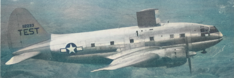 A C-46, a large two engine, propeller driven low-wing airplane. It is modified for icing flight test, with a large (8 ft. by 5 ft.) test airfoil is mounted on top of the body. 'TEST' is emblazened on the tail.
